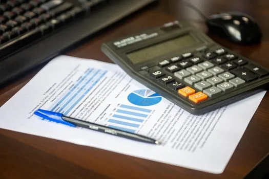 Car owner comparing warranty period and mileage numbers on printed contract with calculator and calendar, realistic automotive finance desk photo